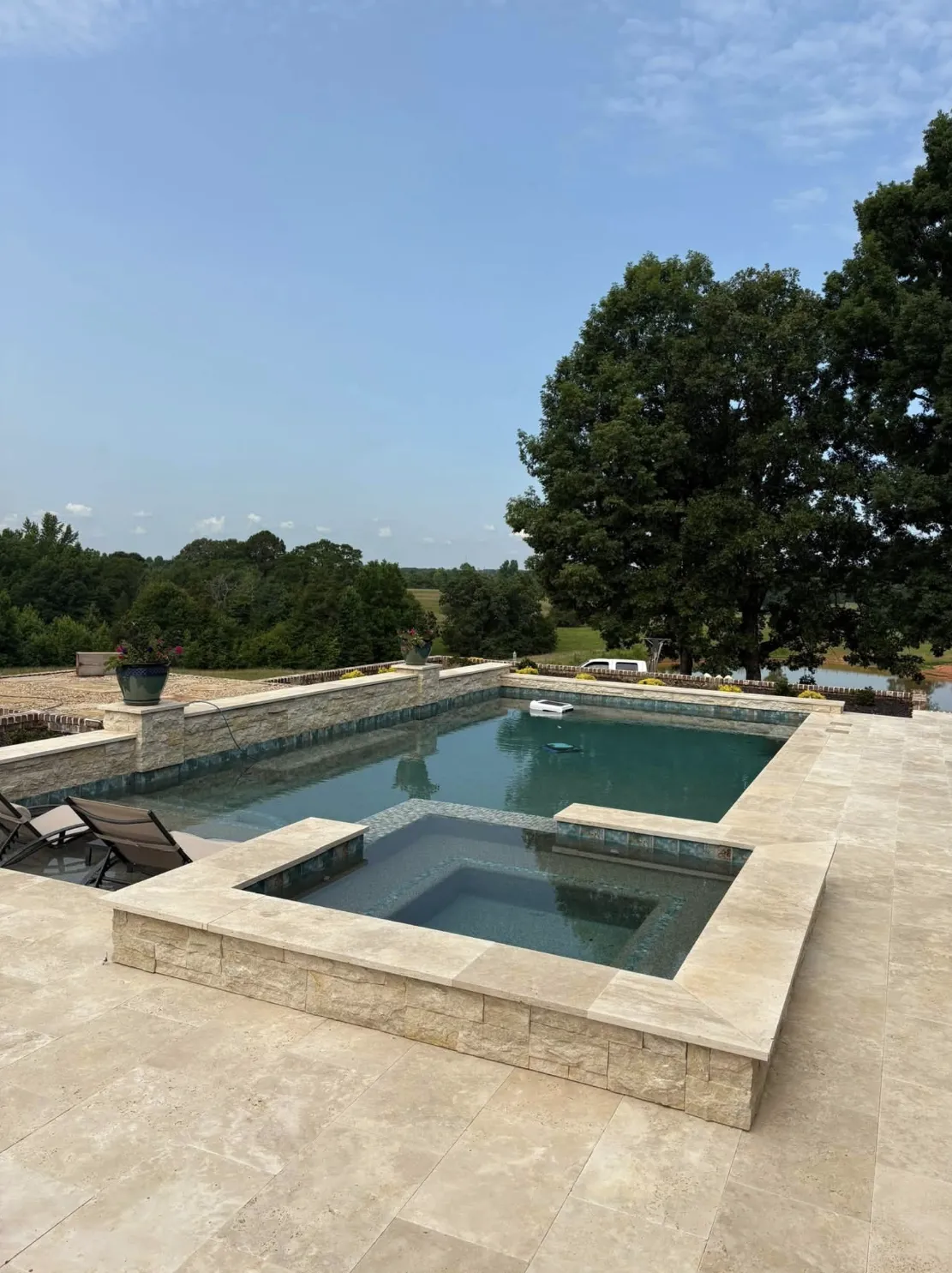 Square pool with raised stacked-stone spa and travertine deck overlooking the Upstate countryside