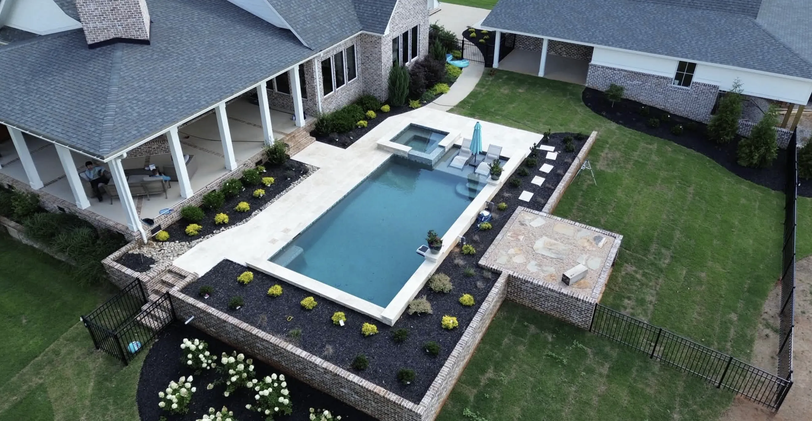 Aerial view of a rectangular pool and spa framed by brick retaining walls and full landscaping