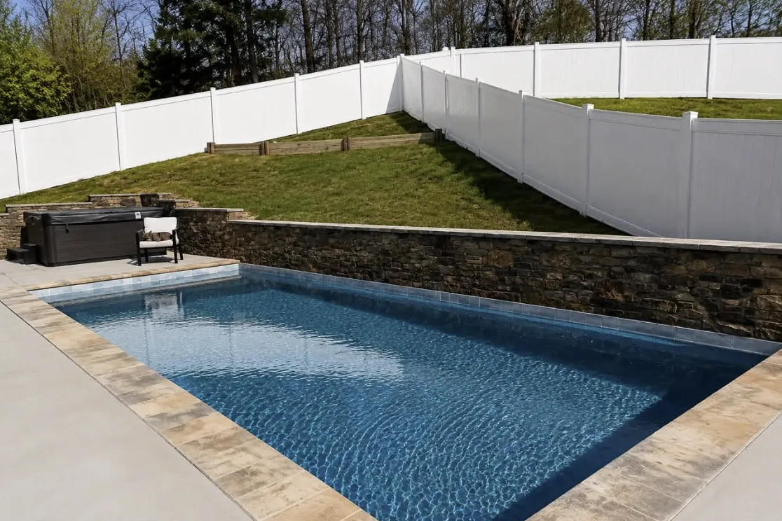 Rectangular pool with a dark stacked-stone wall and white vinyl privacy fence