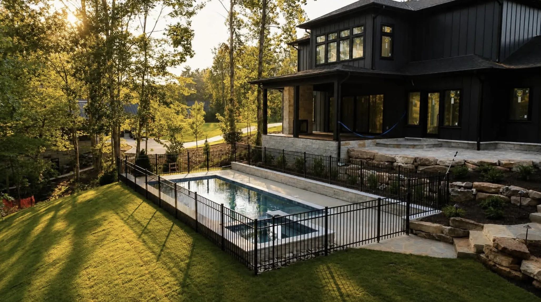 Modern dark two-story home with a sleek rectangular pool and spa at dusk, built by Fireside Pools in the Upstate of South Carolina