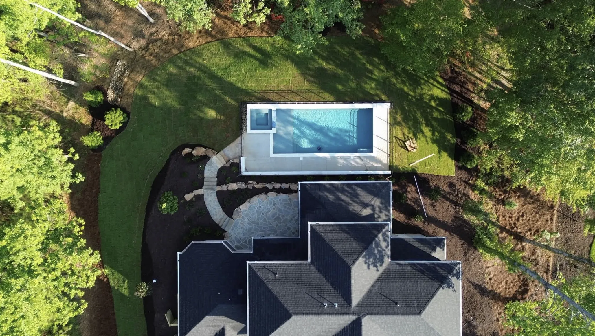Aerial view of a Fireside Pools backyard build, showing the finished pool, patio, and stone pathways nestled among trees